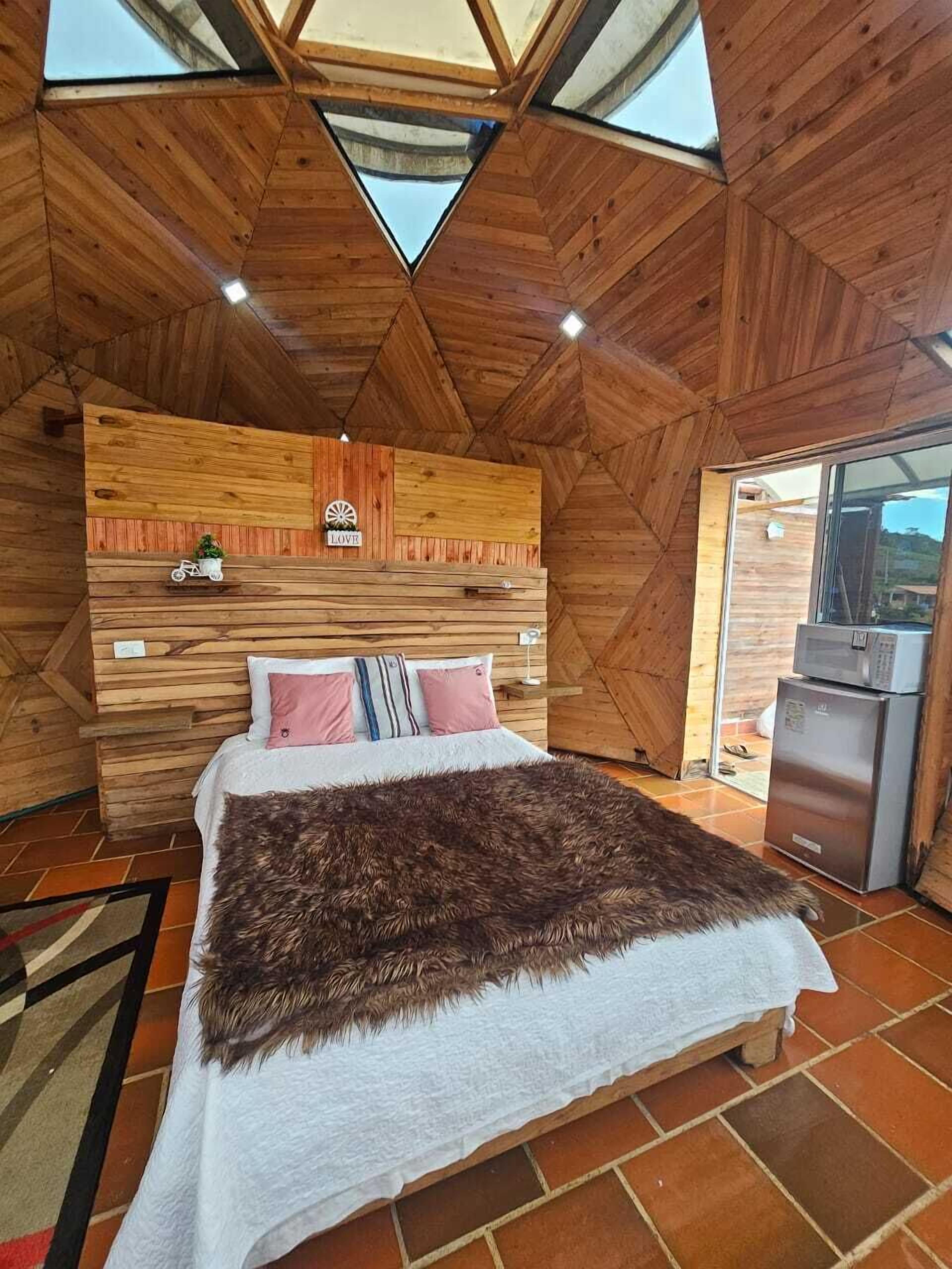 Una habitación de madera con una cama, una mesita y un refrigerador.