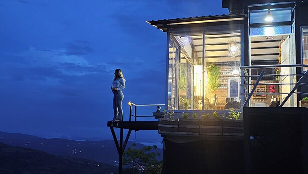 Una persona de pie en un balcón con vistas a un paisaje montañoso de noche.