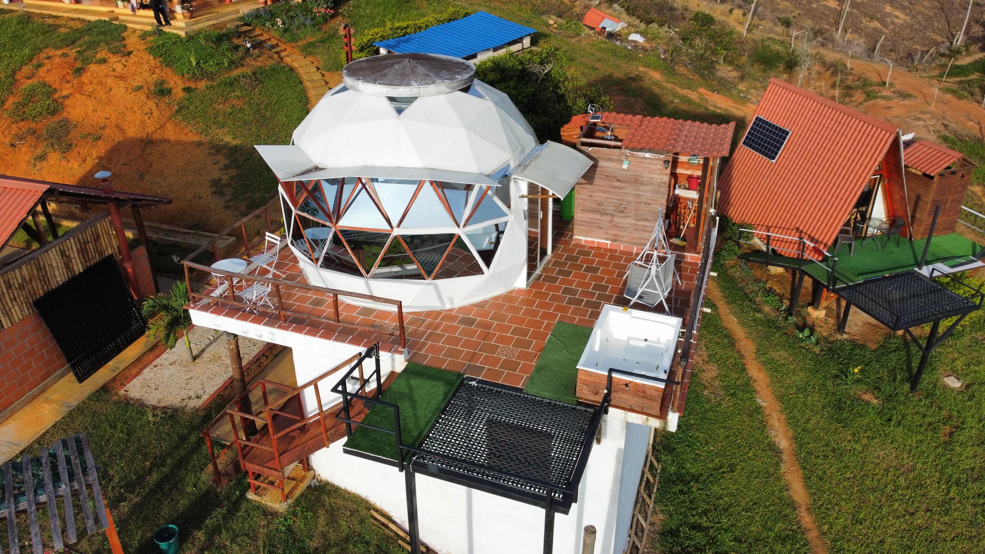 A modern house with a unique dome-shaped structure, a patio with outdoor furniture, and a small garden area.