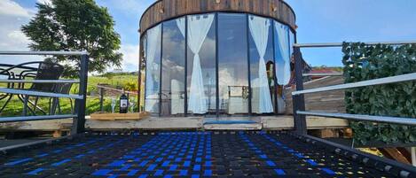 Un bâtiment circulaire doté d’une façade en verre, d’une terrasse en bois et d’une rambarde en métal.