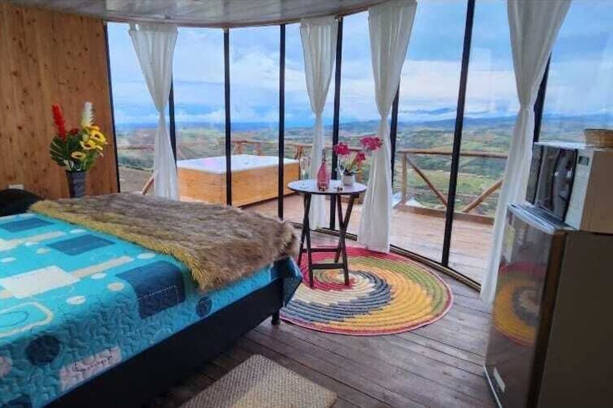 A bedroom with a bed, a small table, a chair, and a view of the landscape.