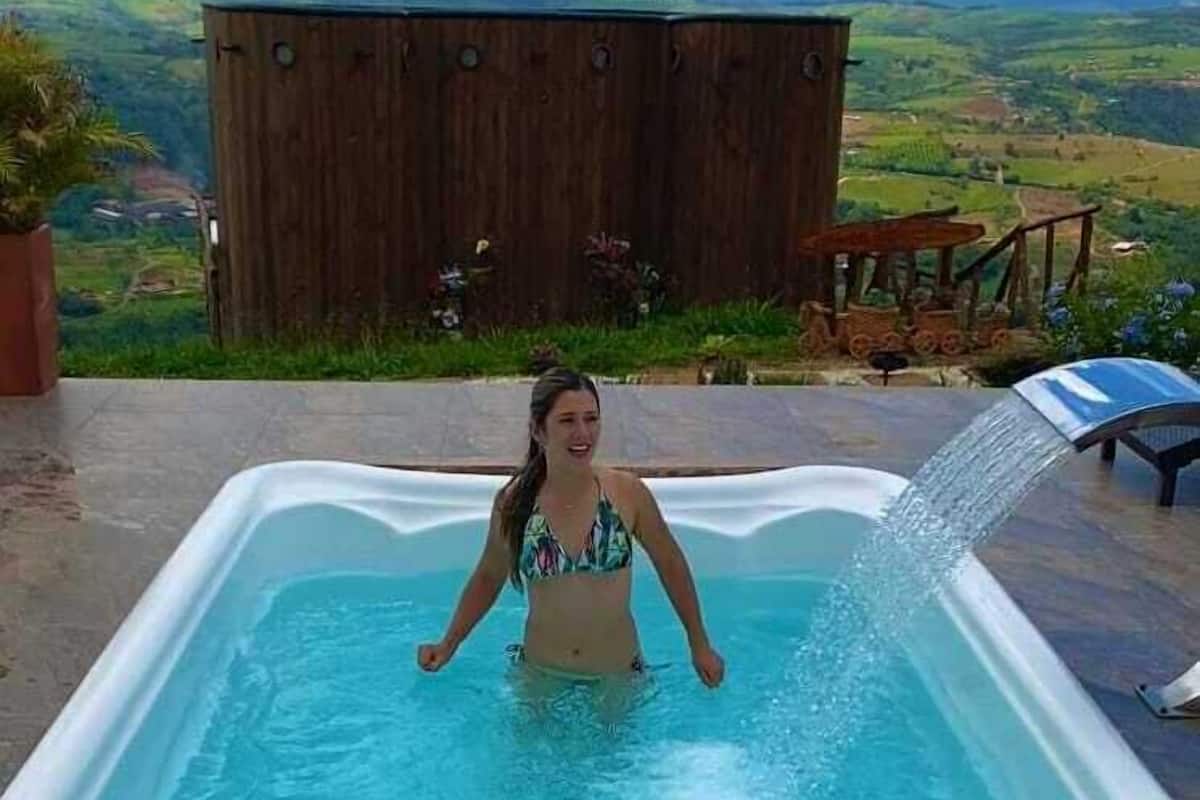 A person in a swimming pool with a view of a wooden structure and a landscape in the background.