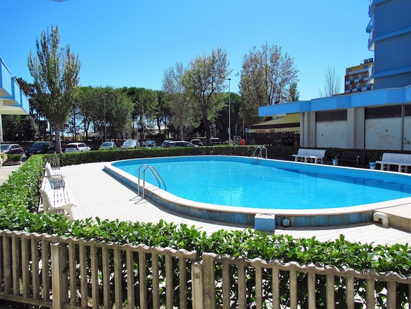 A swimming pool with a wooden fence, benches, and a paved area.
