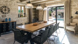 Comedor con pared de piedra, mesa de madera, sillas de mimbre e iluminación colgante.