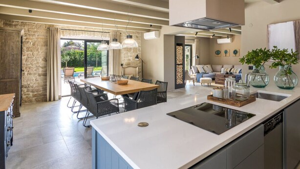Una cocina moderna con una isla central, comedor con sillas y vistas a un patio exterior.