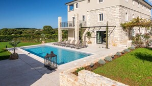 Una casa de piedra de dos pisos con piscina, mobiliario de exterior y jardín.