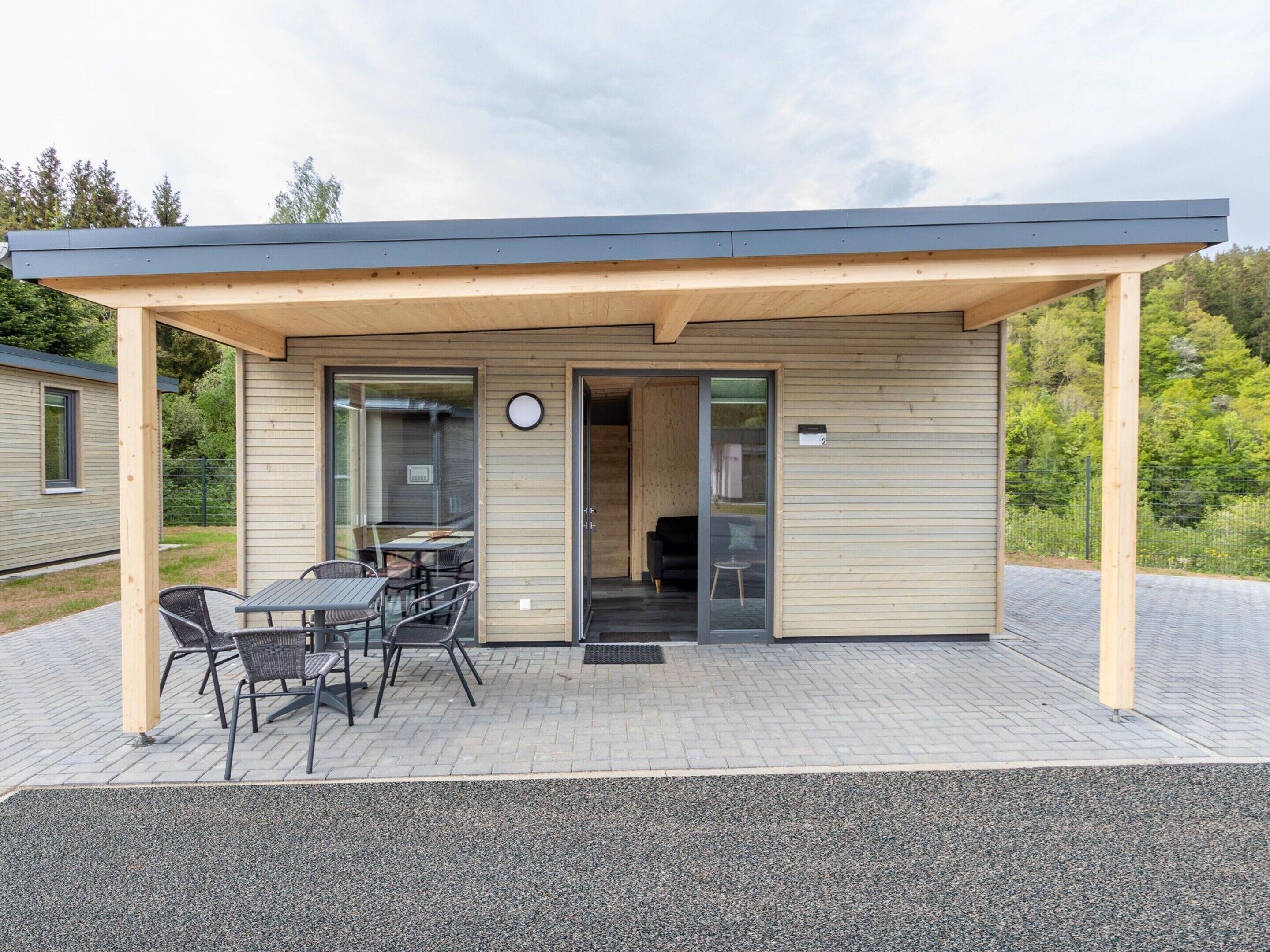 A small, modern building with a covered patio area, featuring a table and chairs, and a door leading inside.