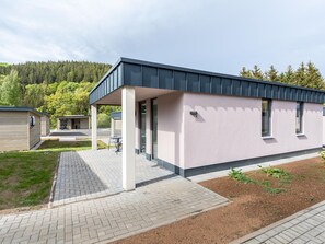 En modern byggnad med en täckt uteplats, ett litet utomhusområde med sittplatser och en asfalterad gångväg som leder till entrén.