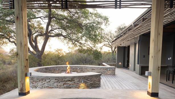 A pool area with a circular stone fire pit, wooden deck, and a pergola structure. - Villa in Hoedspruit With Hot Tub (Hoedspruit)