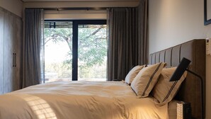 A modern bedroom with a large bed, a bedside table, and a window with curtains. - Villa in Hoedspruit With Hot Tub (Hoedspruit)