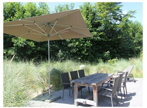 An outdoor dining area with a wooden table and chairs, a large umbrella, and a metal pole.