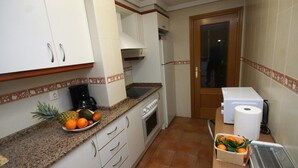 Una cocina compacta con gabinetes blancos, encimera de granito, cafetera, microondas y un refrigerador pequeño.