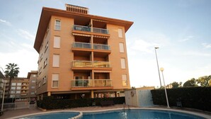 Un edificio residencial de varios pisos con balcones, piscina y jardín ajardinado.