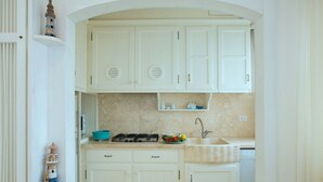Een compacte keuken met witte kastjes, een gasfornuis, een spoelbak en een klein aanrecht met een schaal fruit.