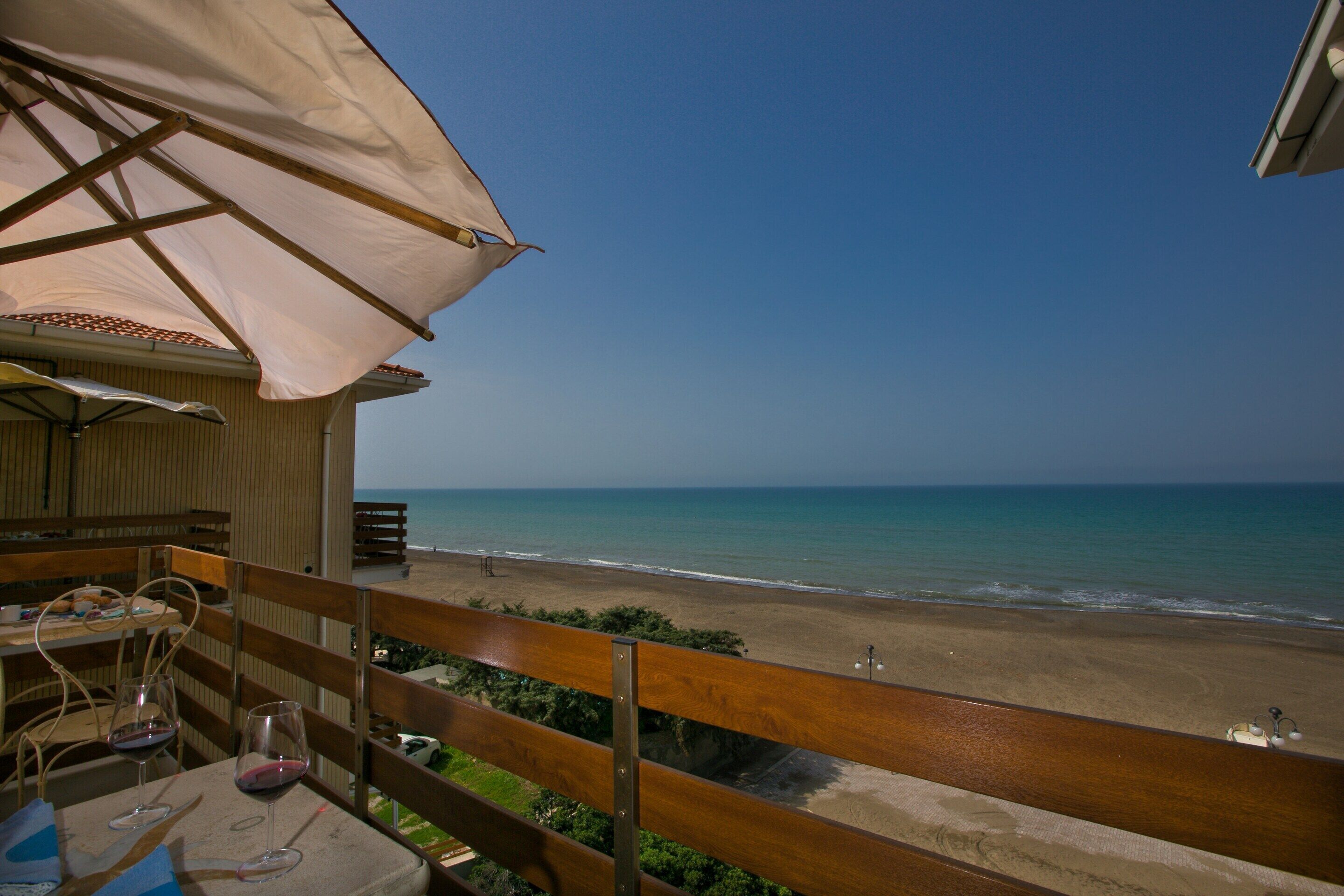 A balcony with a view of the beach, wooden furniture, and a table with wine glasses.