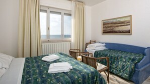 Een hotelkamer met twee bedden, een raam met gordijnen, een schilderij aan de muur en uitzicht op zee.
