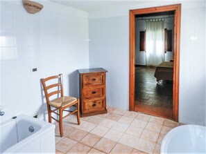 Um banheiro com azulejos brancos, uma cadeira de madeira, um penteado de madeira e uma banheira.