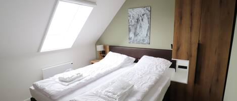 A bedroom with a bed, a window, a wooden wardrobe, and a painting on the wall.