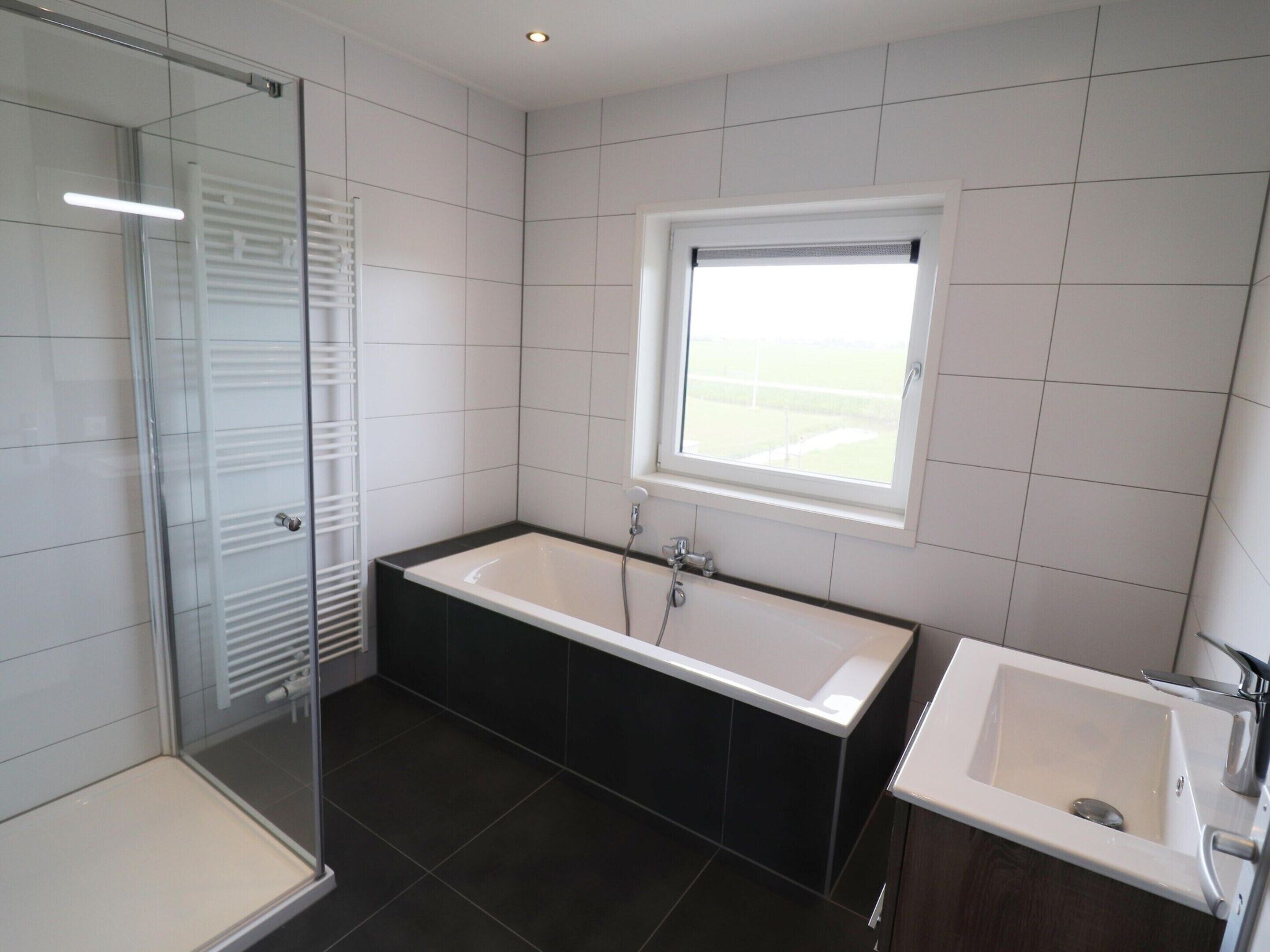 Un baño moderno con cabina de ducha de vidrio, una bañera grande y una ventana que deja entrar luz natural.