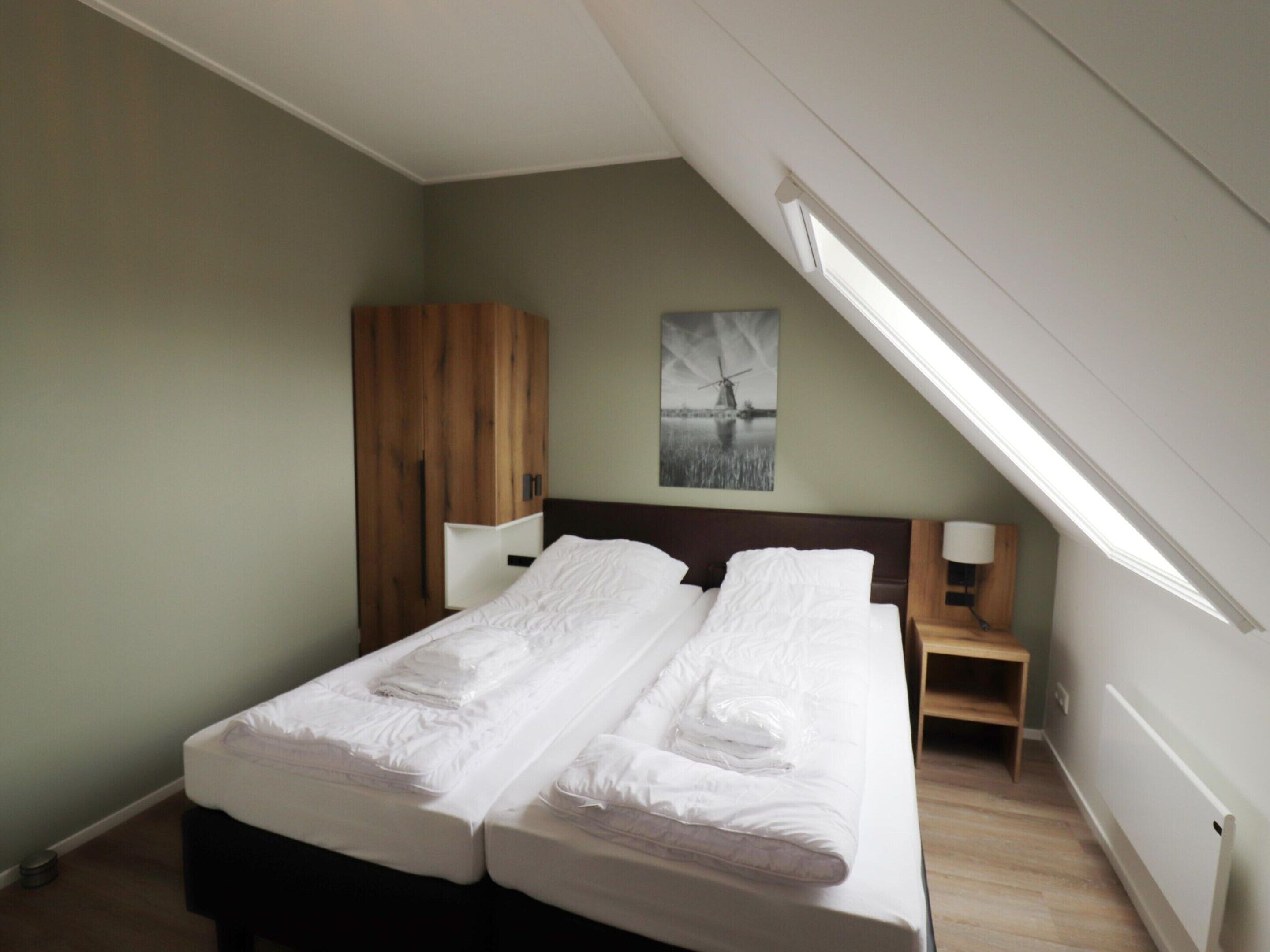 Ein Schlafzimmer mit einem Bett, einem Holzschrank, einem Nachttisch, einer Lampe und einem Bild an der Wand.