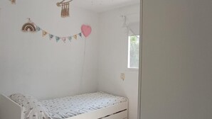A small, single-bed room with a white bed, a window, and a wall decoration of a heart and a string of flags. - Belvilla by OYO Casa El Pinar (Torremolinos)
