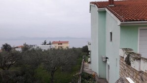 A building with a red-tiled roof, a light green exterior, and a view of a body of water in the background. - Apartments Kozino - Two Bedroom Apartment (Zadar)