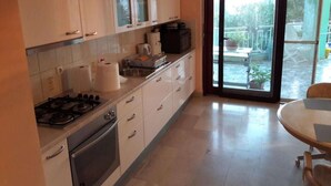 A kitchen with white cabinets, a stove, and a dining table with chairs. - Apartments Kozino - Two Bedroom Apartment (Zadar)