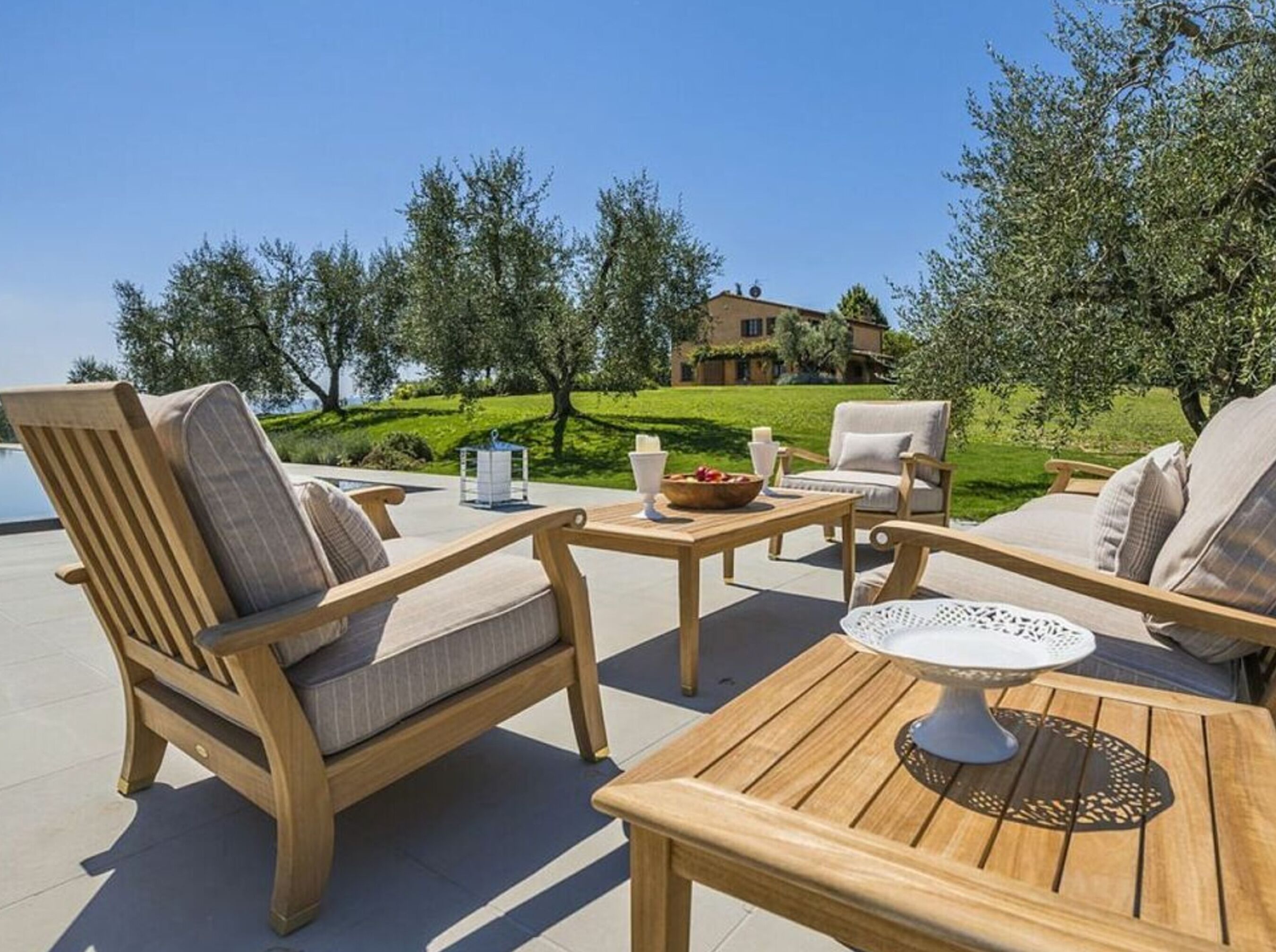 Ein Sitzbereich im Freien mit Holzmöbeln, einem Tisch mit einer dekorativen Mittelstück und Blick auf ein Haus im Hintergrund.