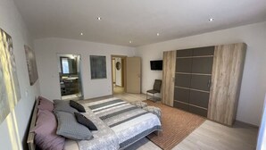 A modern bedroom with a large bed, a wardrobe, a television, and a bathroom visible through an open door. - New White Villa, 60 m2, Pool (Vodnjan)