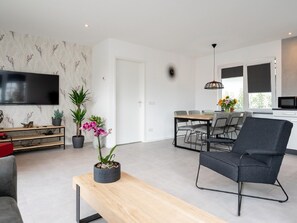 A modern living room with a flat-screen TV, a wooden bench, a grey sofa, and a dining area with a table and chairs. - Beautiful Holiday Home Near Alkmaar (Hensbroek)
