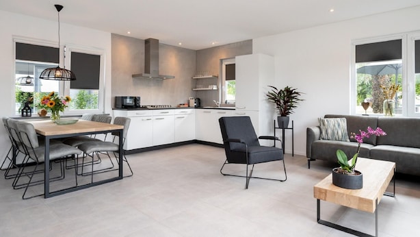 A modern kitchen with white cabinets, a dining area with a wooden table and chairs, a black chair, a grey sofa, and a coffee table with a potted plant. - Beautiful Holiday Home Near Alkmaar (Hensbroek)