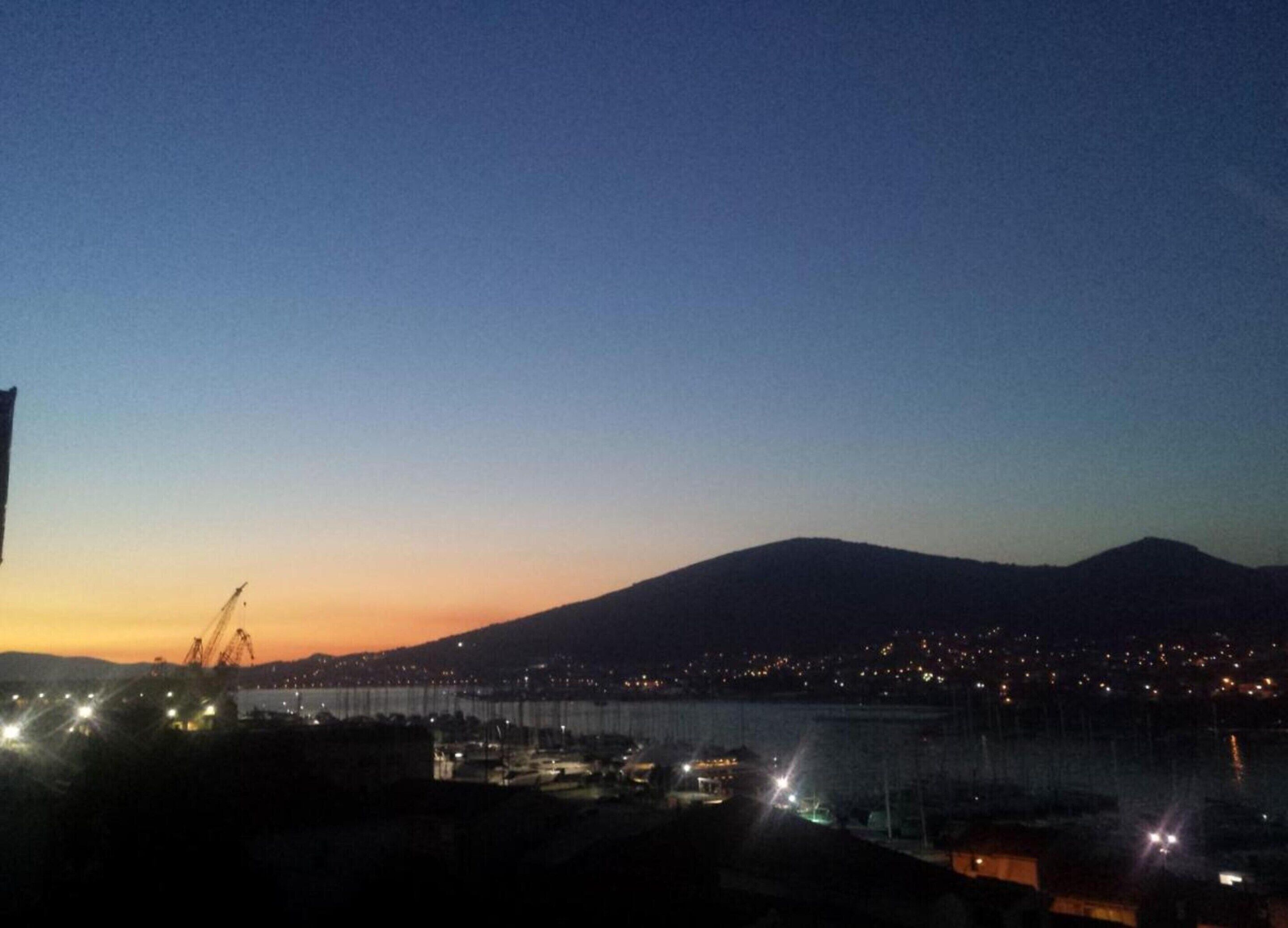 A nighttime view of a cityscape with a mountain in the background and a body of water in the foreground.