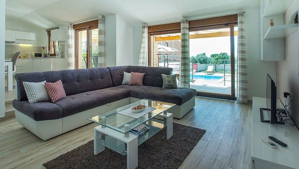A modern living room with a sectional sofa, a glass coffee table, and a view of a swimming pool through large sliding doors. - Villa Monteci Comfortable Holiday Residence (Vodnjan)