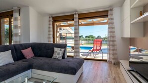 A modern living room with a sectional sofa, a glass coffee table, and a TV on a stand. There is a sliding glass door leading to a pool area. - Villa Monteci Comfortable Holiday Residence (Vodnjan)