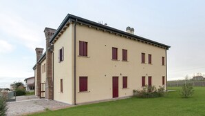 A two-story building with a beige facade, multiple windows with red shutters, and a brick chimney. - Belvilla by OYO Casa Rosolina Due (Ariano nel Polesine)