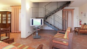 A living room with a television, wooden furniture, a staircase, and a fire extinguisher. - Belvilla by OYO Casa Rosolina Due (Ariano nel Polesine)