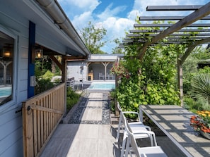 A pool area with a wooden deck, a pergola, and a seating area with chairs.
