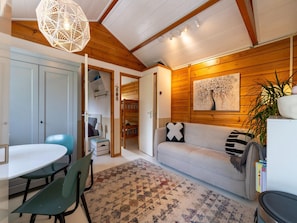 A cozy living room with a wooden ceiling, a dining area with a table and chairs, and a sofa with a decorative pillow.