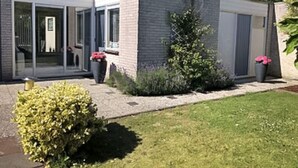 A modern two-story house with a brick exterior, large sliding glass doors, and a small garden with a bush and two flower pots. - Huijsmans Verhuur Type A de Luxe Grevelingen 29 (Ouddorp)