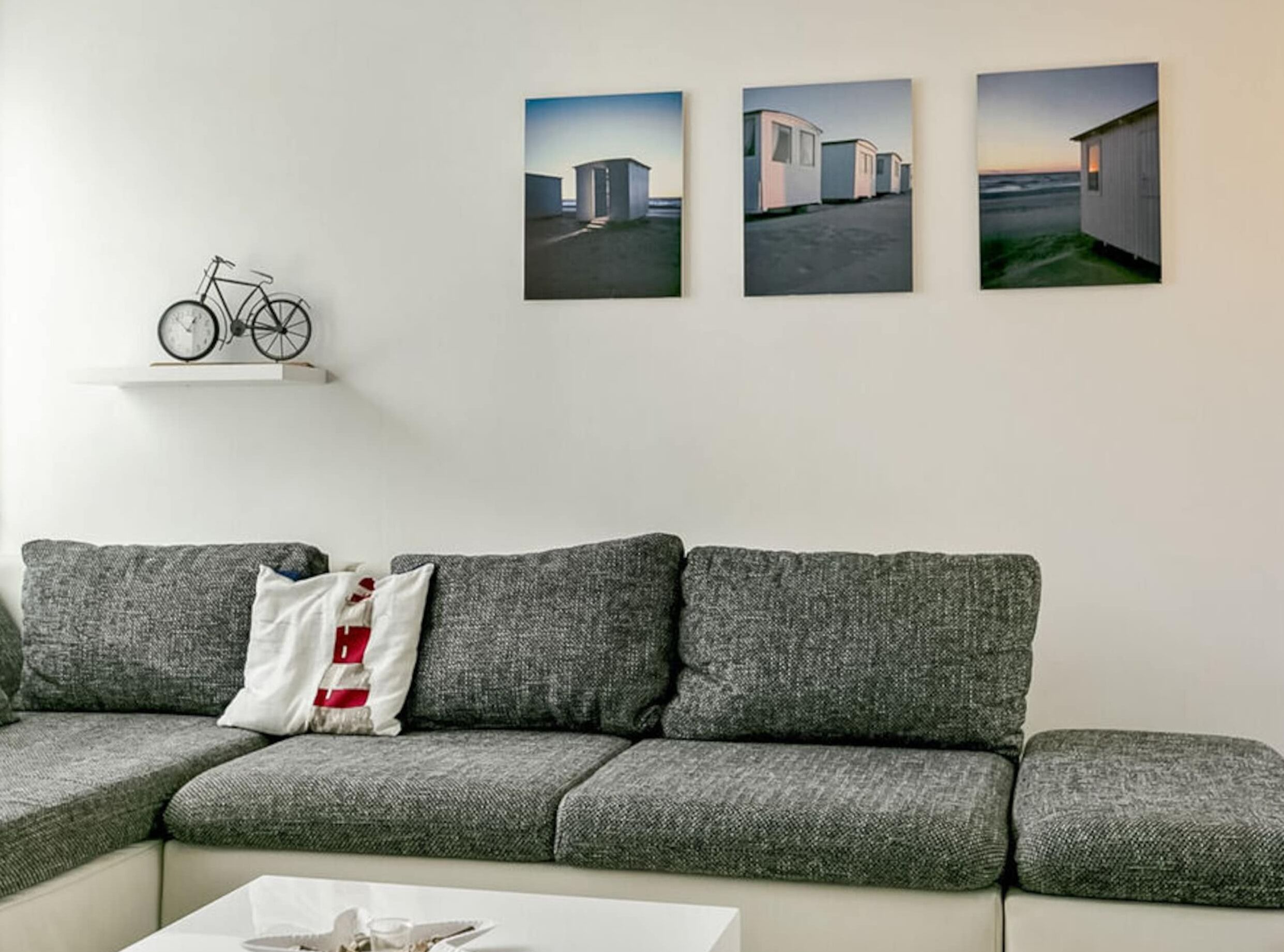 Un salon avec un canapé gris, une table basse blanche et trois tableaux encadrés accrochés au mur.
