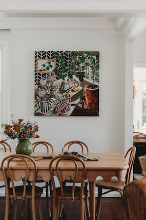 Un comedor con una mesa y sillas, un cuadro en la pared y un florero con flores sobre la mesa.