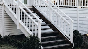 A white house with a staircase leading to a deck.