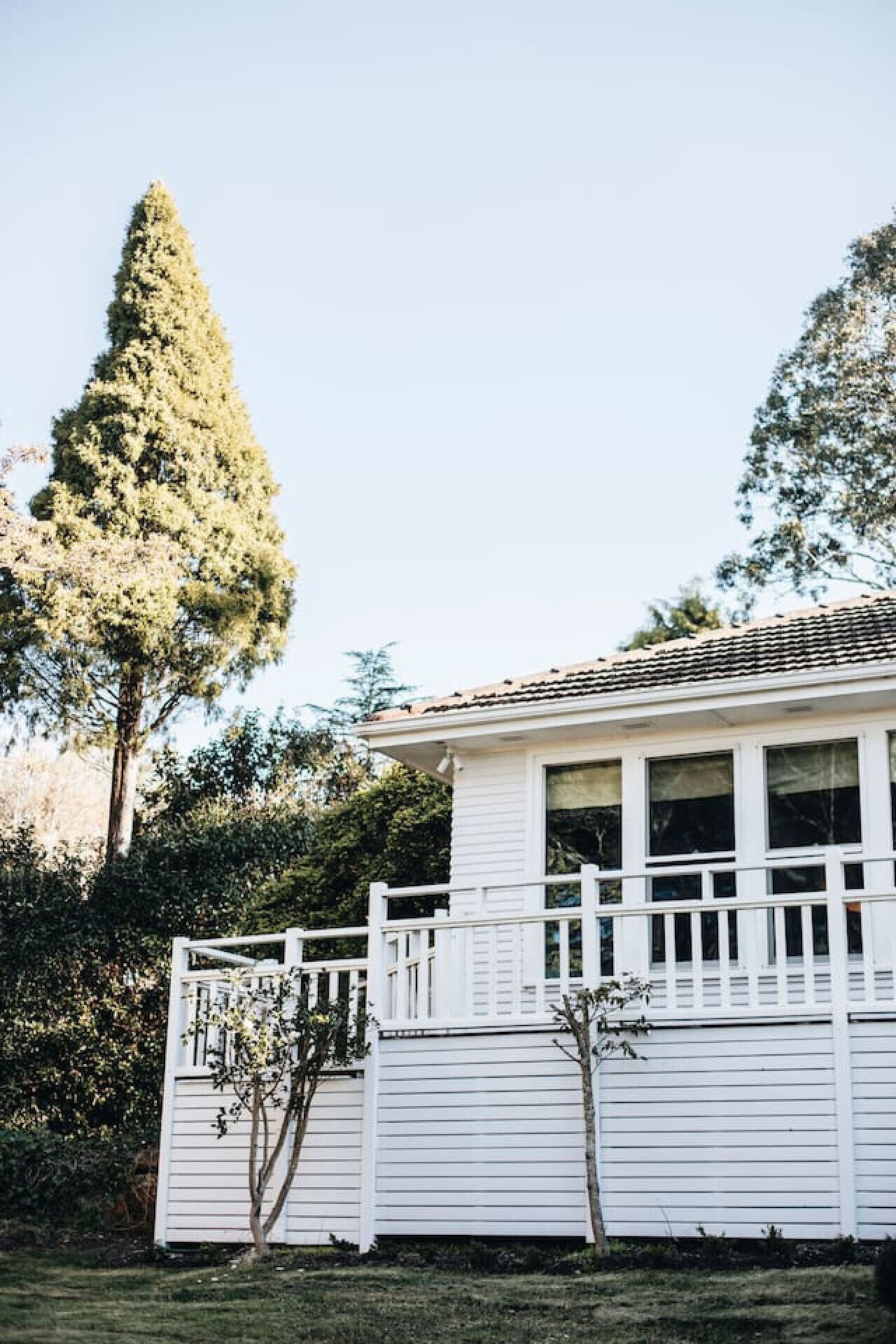 Une maison blanche d’un seul étage, dotée d’un porche à l’avant, entourée d’arbres et sous un ciel dégagé.