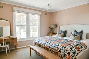 Un dormitorio con una cama grande, un escritorio, una silla y una ventana con vistas a árboles.