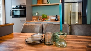 A modern kitchen with a dining table set for two, featuring a teal candle, a glass candle holder, and a clear glass. - Holiday Home in Voorthuizen Near Veluwe Park (Voorthuizen)