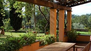 An outdoor patio with a wooden table and bench, surrounded by lush greenery and a pergola structure. - Spacious Tuscan Villa Retreat (Palaia)