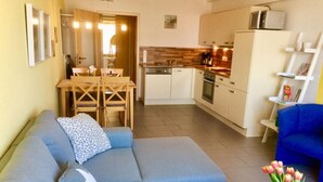 A modern living room with a sofa, a dining table, and a kitchen area with cabinets and appliances. - Beach Dune 18 on the Beach (Karlshagen)