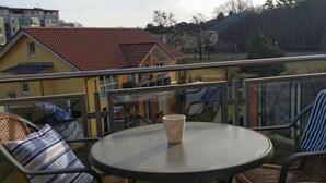 A balcony with wicker furniture, a round table, and a view of buildings and trees. - Beach Dune 18 on the Beach (Karlshagen)