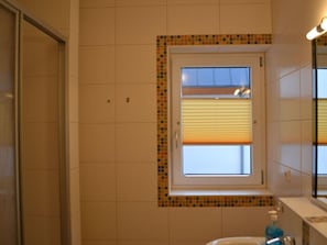 Un baño con ventana, paredes enlosadas y un lavabo con dispensador de jabón.