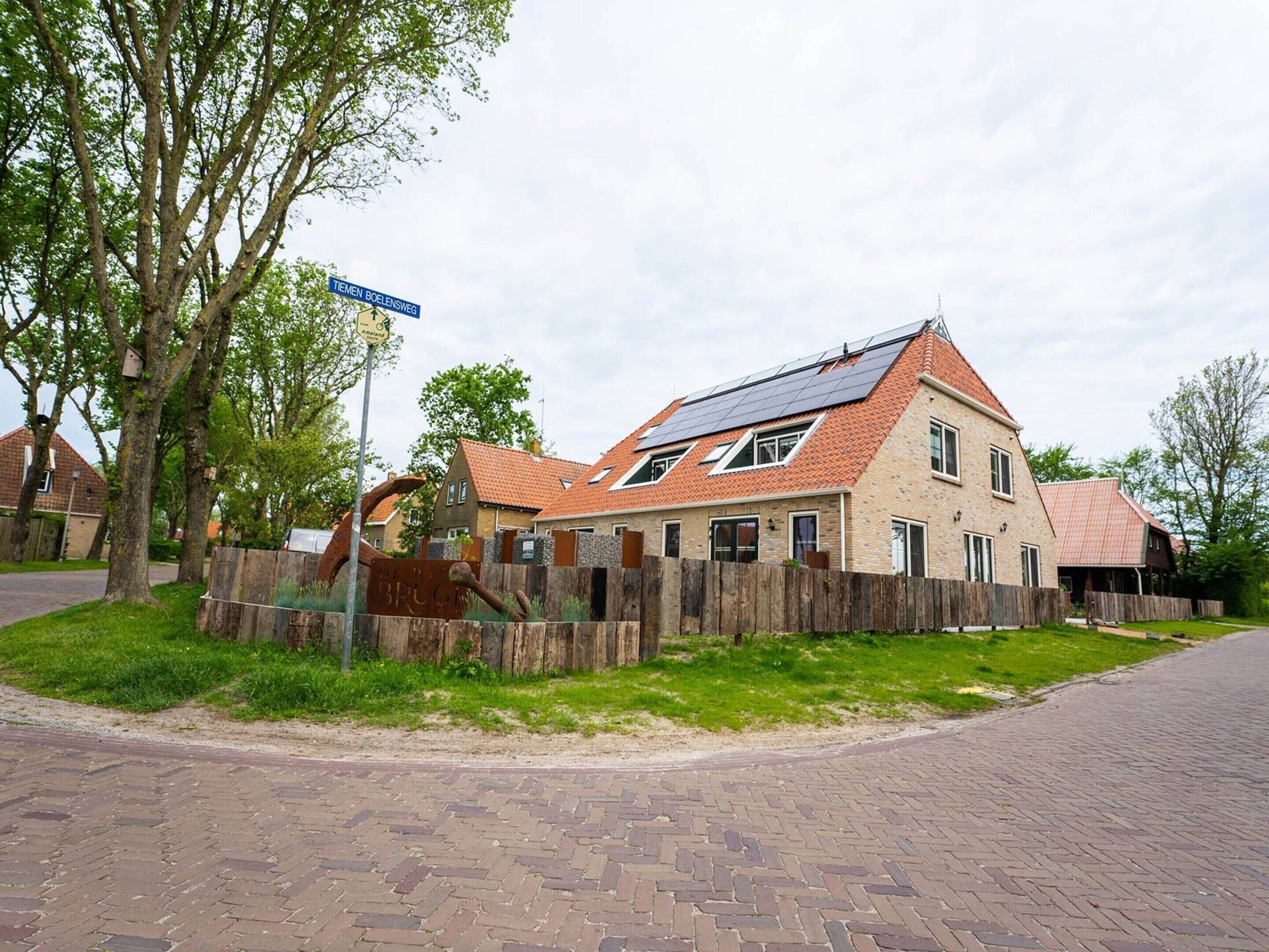 Une maison à deux étages avec un toit en pente, des panneaux solaires et une clôture en bois.